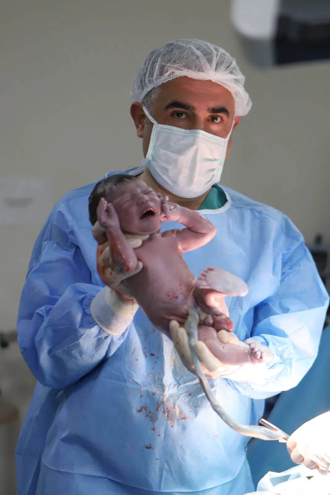 Mavi önlüklü Op. Dr. Hayri Aksüt yenidoğanla ameliyathanede