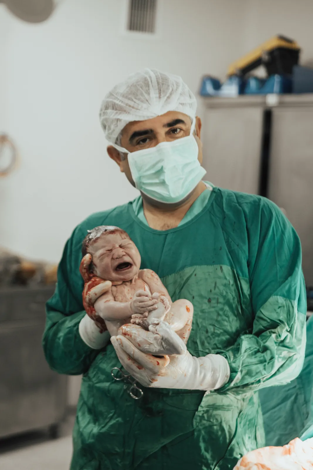 Yeşil önlüklü Op. Dr. Hayri Aksüt doğum sonrası bebekle