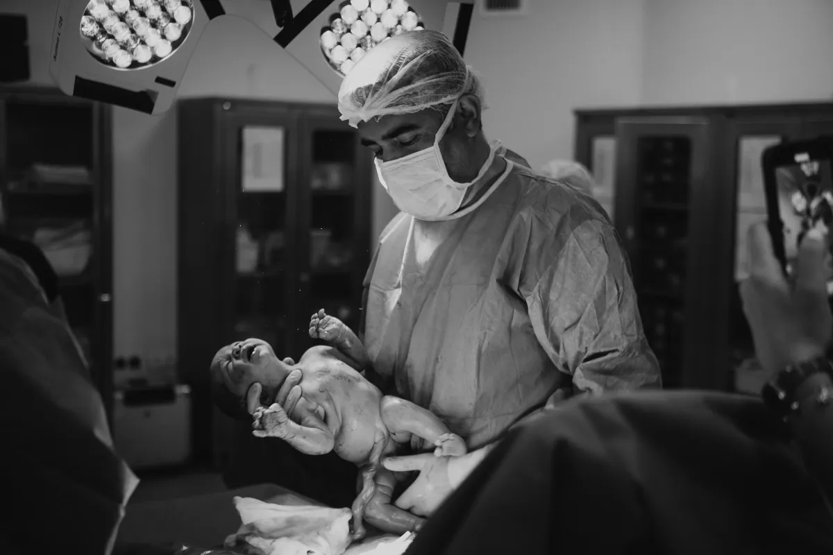 Doğumdan hemen sonra annenin yanında yenidoğanı tutan Op. Dr. Hayri Aksüt